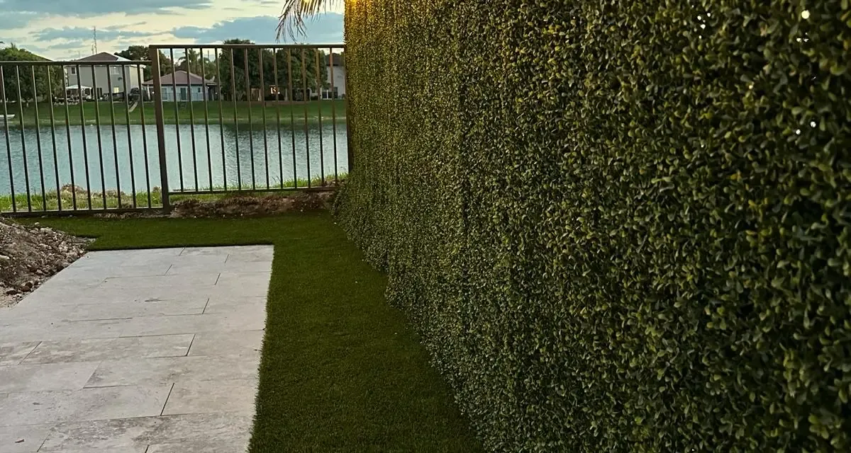String lights glowing at dusk over a lush green synthetic hedge and lawn, set up for evening entertaining