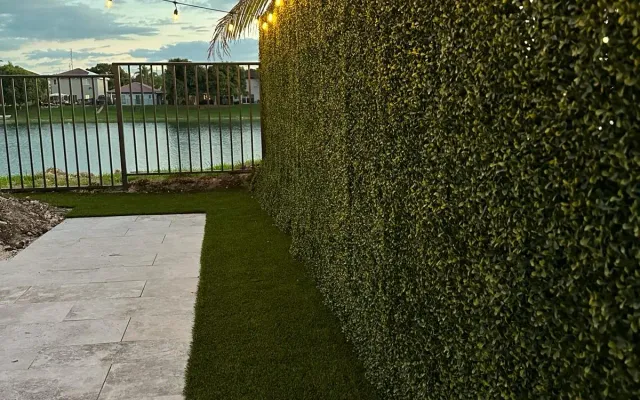 String lights glowing at dusk over a lush green synthetic hedge and lawn, set up for evening entertaining