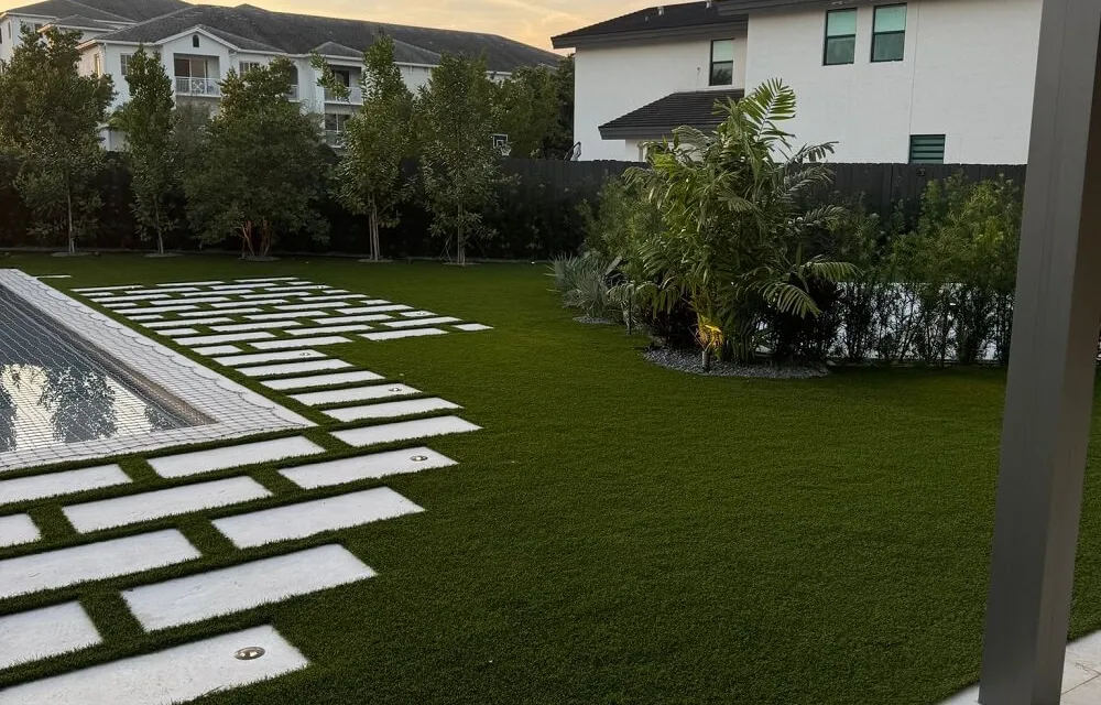 Paver patio bordered by a neat artificial turf lawn with tropical landscaping
