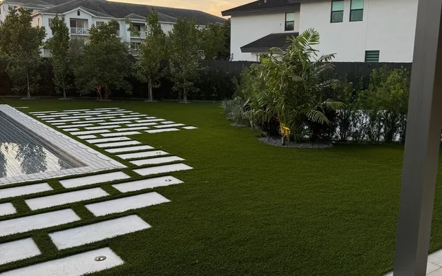 Paver patio bordered by a neat artificial turf lawn with tropical landscaping