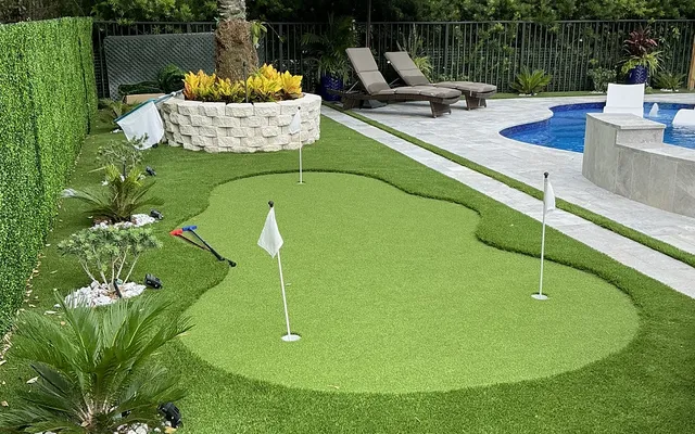 Backyard putting green beside a pool with palm trees in the background