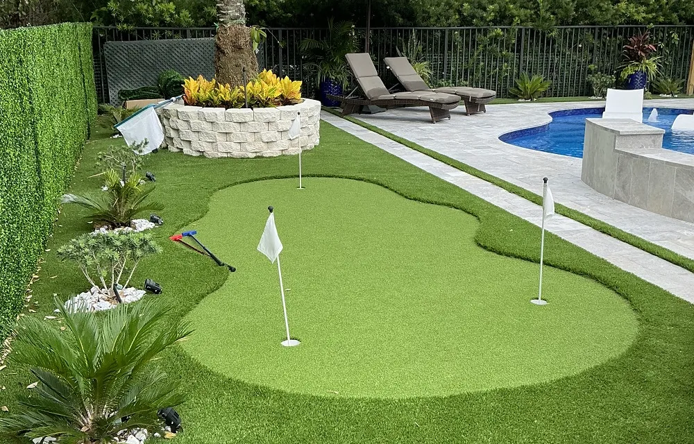 Backyard putting green beside a pool with palm trees in the background