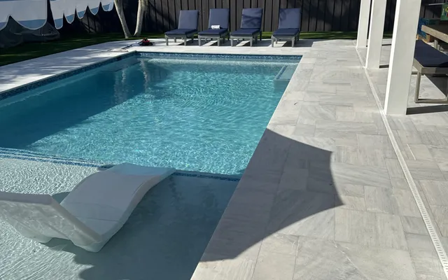 Estate-style pool patio bordered by a manicured artificial lawn