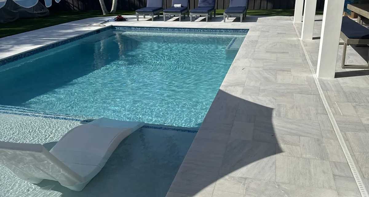 Estate-style pool patio bordered by a manicured artificial lawn